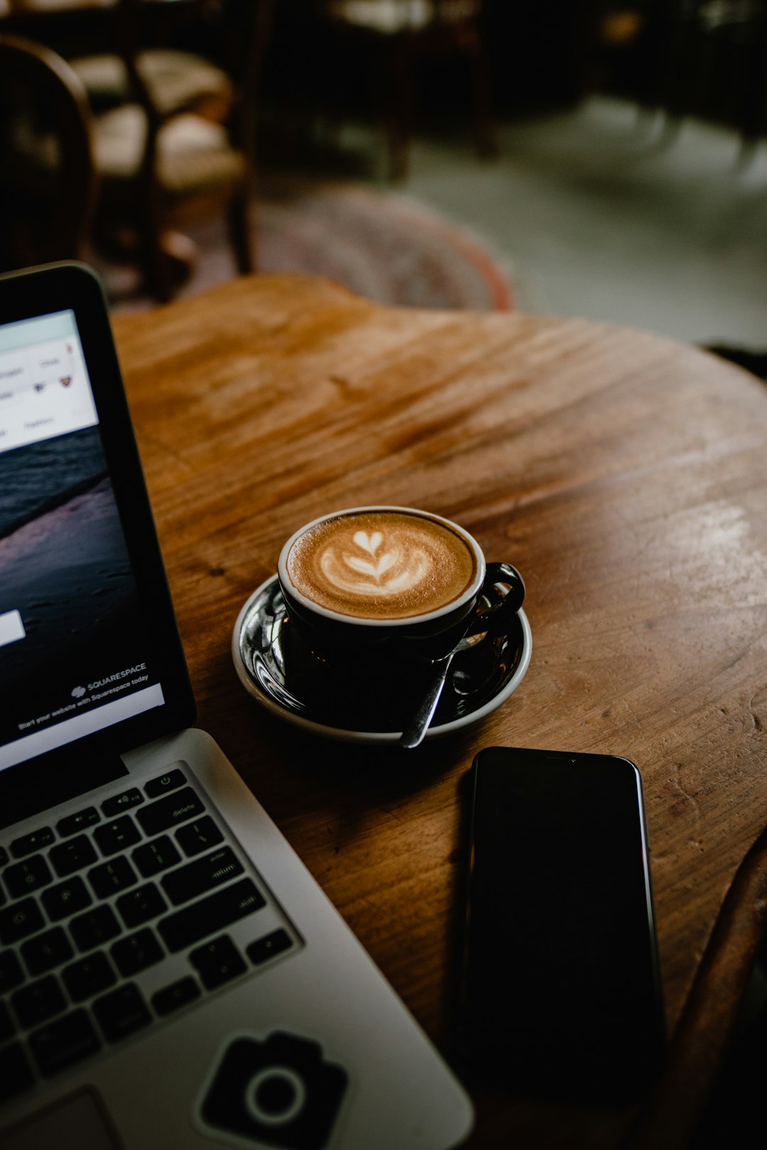 Flat white in a black cup beside a laptop on a wooden table